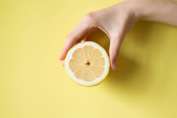 Lemon in woman's hand on a yellow background - Zdjęcie, obraz