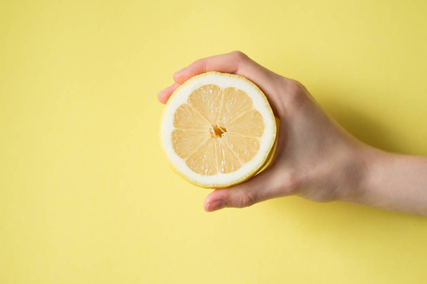 Lemon in woman's hand on a yellow background - Φωτογραφία, εικόνα
