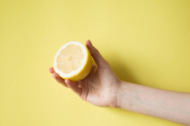 Lemon in woman's hand on a yellow background - Foto, afbeelding