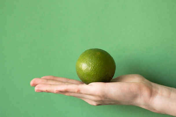 Fresh juicy tasty green lime in a human hand on green background - Фото, зображення