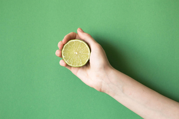 Fresh juicy tasty green lime in a human hand on green background - Fotografie, Obrázek