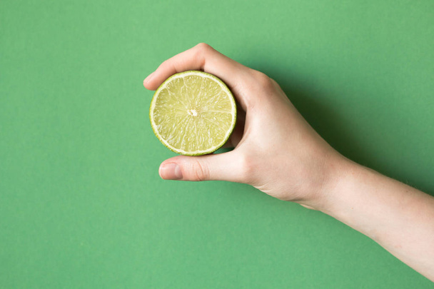 Fresh juicy tasty green lime in a human hand on green background - Фото, зображення