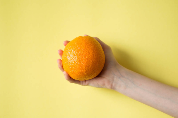 Hand holding orange on yellow background food concept - Foto, afbeelding