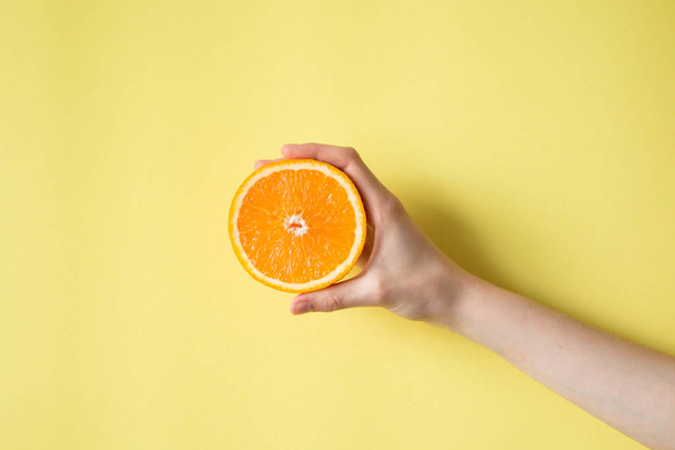 Hand holding orange on yellow background food concept - Фото, зображення