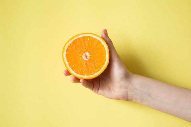 Hand holding orange on yellow background food concept - Photo, image