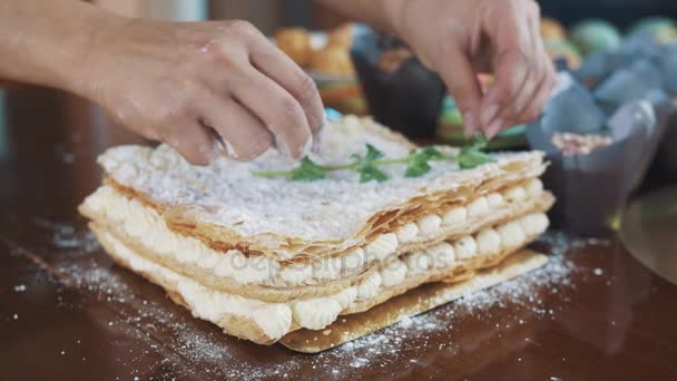Мужские руки украшают слоистый торт, покрытый сахарным порошком со стеблем мяты
 - Кадры, видео