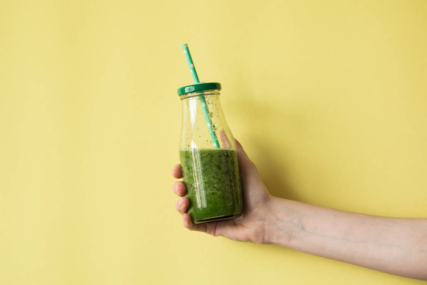 Woman hand holding smoothie shake against colored wall. Drinking green healthy smoothie concept. - Foto, Imagem