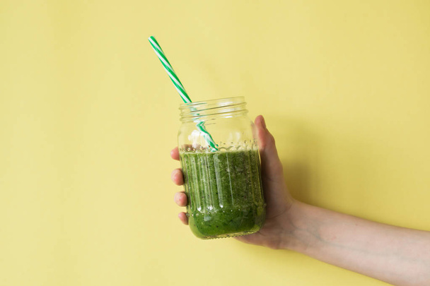 Woman hand holding smoothie shake against colored wall. Drinking green healthy smoothie concept. - Foto, imagen