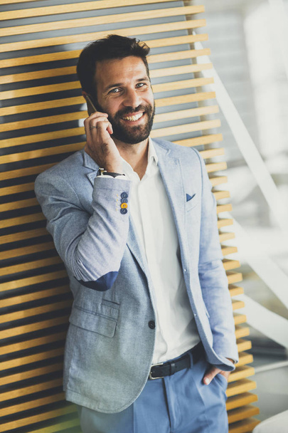 Красивый молодой бизнесмен пользуется телефоном в офисе
 - Фото, изображение