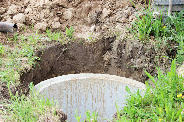 Puits d'extraction d'eau. La construction d'un puits de village pour l'extraction de l'eau à l'aide de plusieurs anneaux de béton posés dans une fosse de terre
 - Photo, image