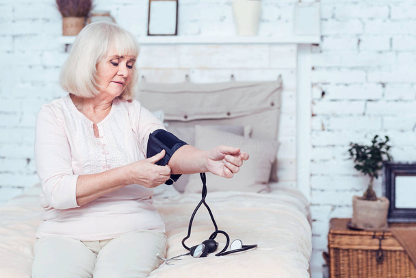 Confident elderly lady measuring blood pressure at home - Valokuva, kuva