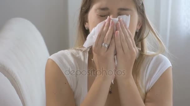 Mujer enferma joven sentada en el sofá en la sala de estar y estornudando pañuelo de papel
 - Metraje, vídeo
