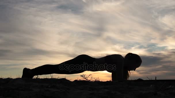 Kobieta robi deski hip twisty na plaży o zachodzie słońca - Materiał filmowy, wideo