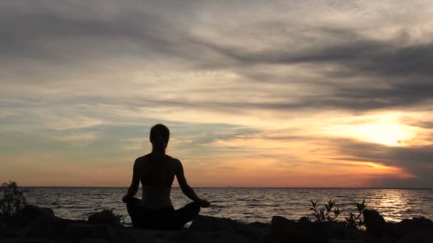 joga kobieta w pozie Lotos na plaży o zachodzie słońca - Materiał filmowy, wideo