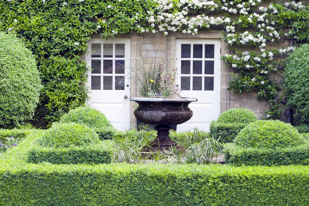 Topiary garden with ornamental plant pot in the middle, in front of stone cottage . - Valokuva, kuva