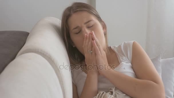 Closeup of young sick woman lying on sofa, coughing and using throat spray - Filmati, video