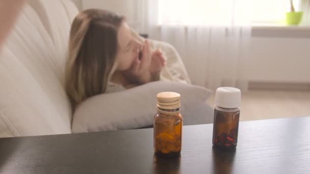 ベッドサイドのテーブルからボトルで薬に手を伸ばす若い病気の女性のクローズ アップ ショット - 映像、動画