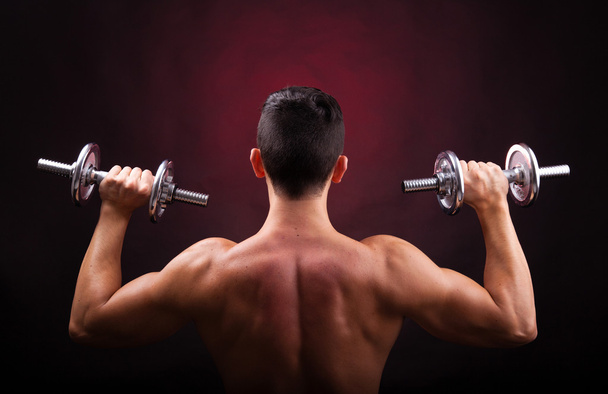 Muscular young man lifting weights from back against black backg - Foto, Imagem