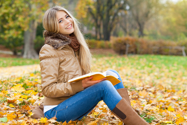 Улыбающаяся женщина читает в парке осенью
 - Фото, изображение