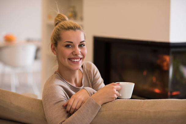 Portrait of beautiful young woman with a mug near a fireplace - 写真・画像