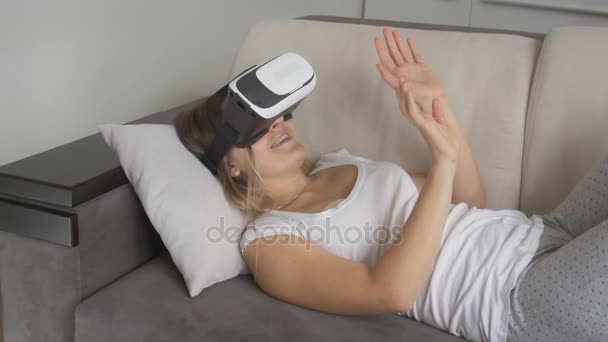 Joven mujer sonriente acostada en la cama y viendo videos de 360 grados con auriculares VR. Filmación en resolución 4K
 - Metraje, vídeo