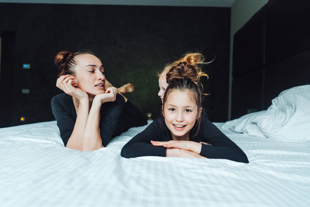 Η μαμά και οι δύο κόρες διασκεδάζουν στο κρεβάτι. - Φωτογραφία, εικόνα