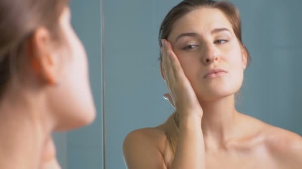 4 k beelden van jonge vrouw haar gezicht voor rimpels op badkamer controleren - Video