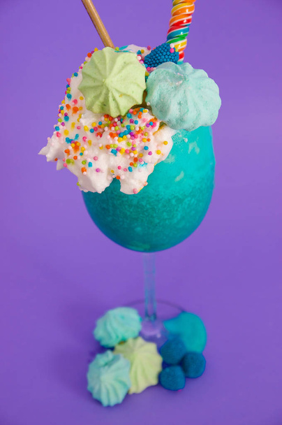 Delicious homemade extreme milkshake with dragees over a milk foam, in a purple background - Фото, зображення