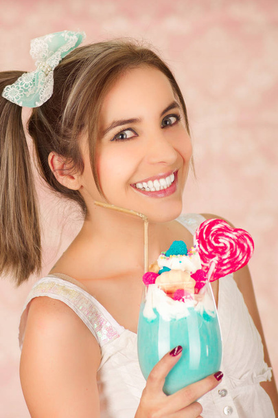 Indoor portrait of pretty cute woman holding a tasty blue milk shake, trendy clothes, studio fashion in a pink background - Φωτογραφία, εικόνα
