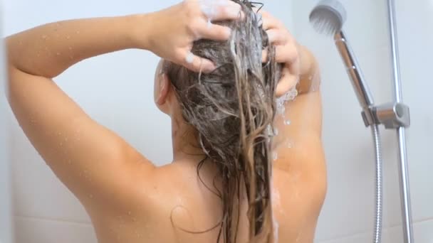 Slow motion rear view shot of sexy brunette woman washing hair with shampoo at shower - Video