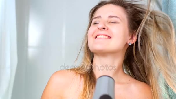 Filmagem em câmera lenta de mulher loira sorridente usando secador de cabelo no banheiro
 - Filmagem, Vídeo