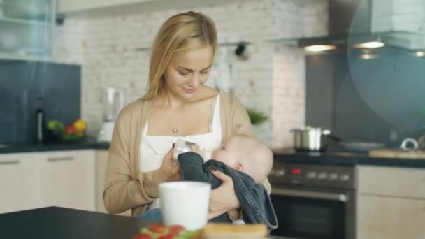 Beautiful Young Mother Feed Her Cute Child from a Bottle. All this is Happening on a Modern Kitchen. - Footage, Video