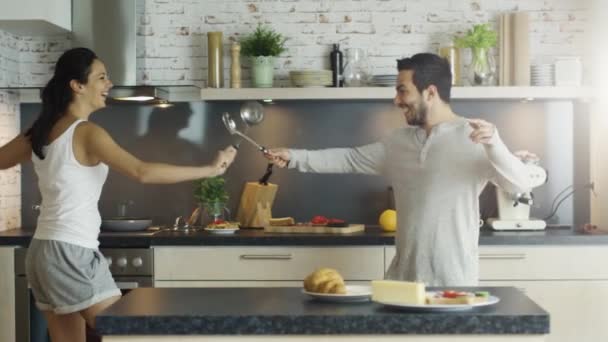 On the Kitchen Young Handsome Couple is Fencing with Kitchen Appliances. On the Stove Something Cooks in the Pan. - Materiał filmowy, wideo