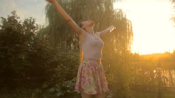 Mulher rindo alegre desfrutando de chuva de verão no jardim ao pôr do sol
 - Filmagem, Vídeo