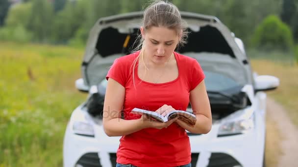 Naštvaná mladá žena čte stojící na auto brokedown a čtení Manula na opuštěné venkovské cestě - Záběry, video