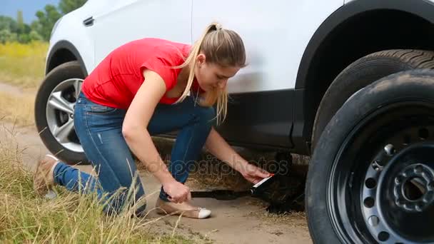 Mladá žena mění pneumatiku na autě rozbité na poli - Záběry, video