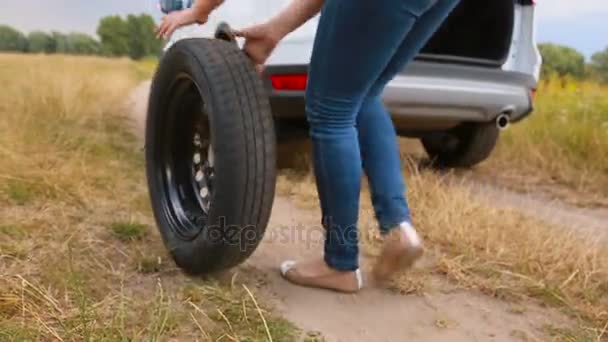 Νεαρή γυναίκα λήψη εφεδρικού τροχού έξω από το αυτοκίνητο και το τροχαίο στο έδαφος - Πλάνα, βίντεο