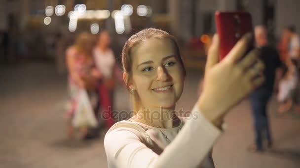 Mulher sorridente bonita fazendo tiro selfie no smartphone na rua da noite
 - Filmagem, Vídeo