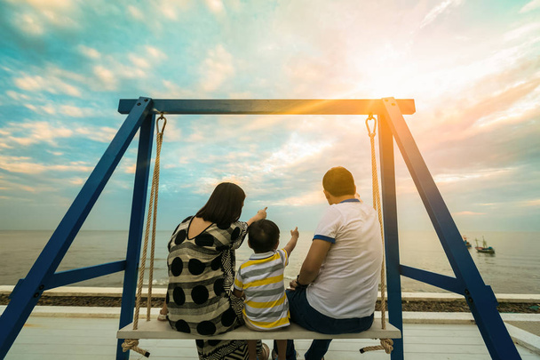 Heureuse jeune famille s'amuser assis swing sur la plage au coucher du soleil
. - Photo, image