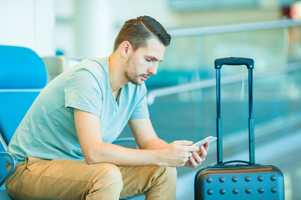 junger Mann in einer Flughafenlounge, der auf ein Flugzeug wartet. Kaukasier mit Smartphone im Wartezimmer - Foto, Bild