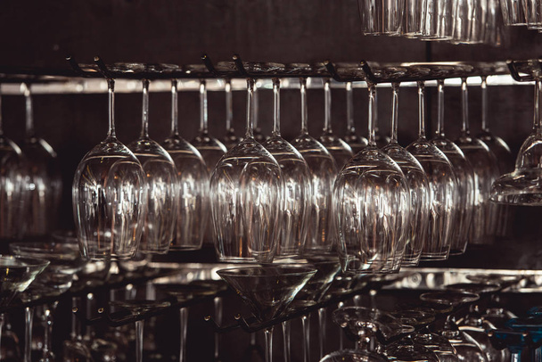 Brillengläser für Margarita, Martini, Grog und Likör hängen kopfüber in Bar im Restaurant, dunkler Hintergrund. - Foto, Bild
