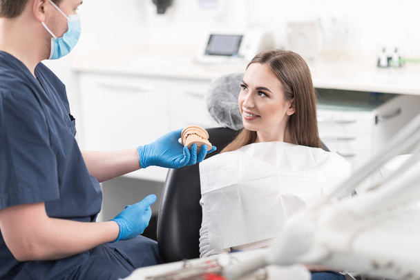 Dentist showing typodont to cheerful patient - Zdjęcie, obraz