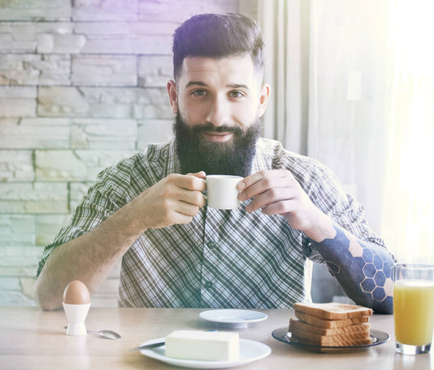 bebaarde man zit aan tafel met ontbijt  - Foto, afbeelding