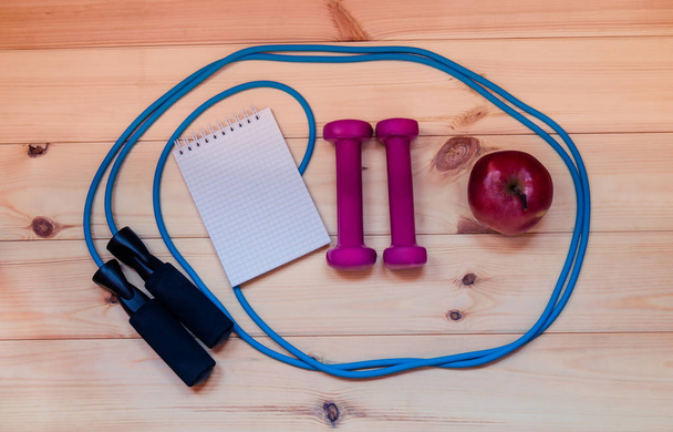 Dumbbells, notebook, apple and skipping rope on wooden background - Photo, Image
