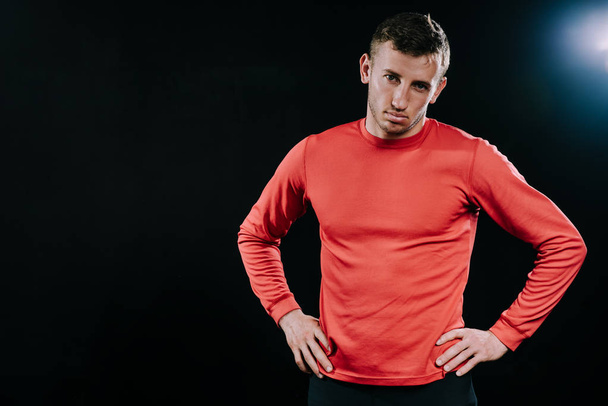 Athlete man in red sportswear standing over dark background, holding hands on his waist. Lifestyle, sport, motivation. - Valokuva, kuva