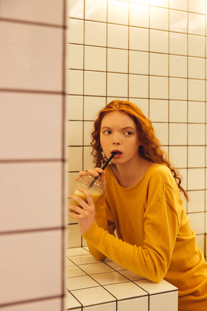 Serious young redhead curly lady sitting in cafe - 写真・画像