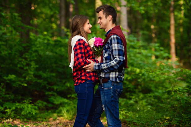 Stylish young couple in shirts and jeans while walking in the forest. A charming girl and her handsome boyfriend are looking at each other. - Fotografie, Obrázek