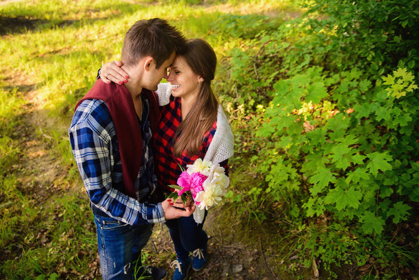 Stylish young couple in shirts and jeans while walking in the forest. The beautiful charming girl and her handsome boyfriend leaned against each other. - Valokuva, kuva
