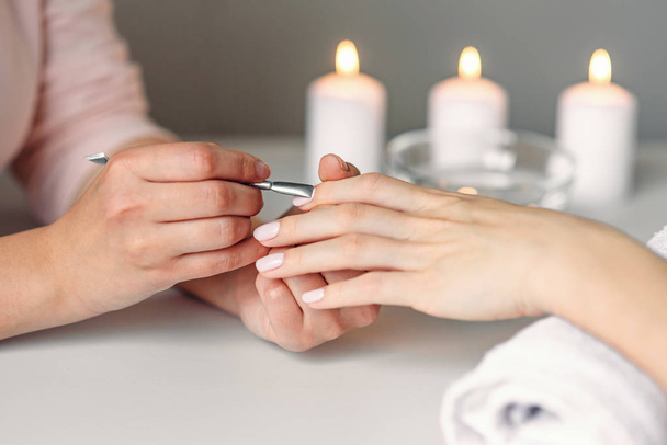 Nail care. Closeup of beautiful woman hands getting manicure in spa salon. Female manicurist cleaning cuticle with professional manicure pusher tool. Cosmetic procedure. - Foto, immagini