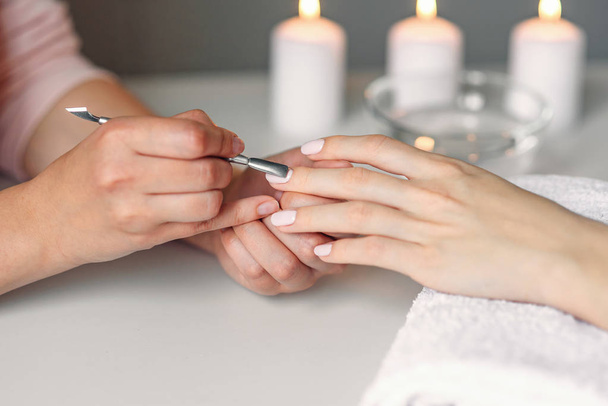 Nail care. Closeup of beautiful woman hands getting manicure in spa salon. Female manicurist cleaning cuticle with professional manicure pusher tool. Cosmetic procedure. - Foto, Imagen